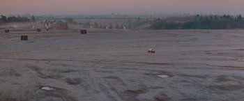 Movie still from “The Adjuster” (1991), directed by Atom Egoyan – A truck driving down a dirt road in a field; Extreme Wide shot, High angle