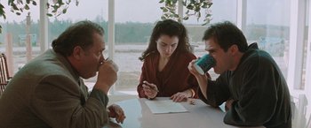 Movie still from “The Adjuster” (1991), directed by Atom Egoyan – A group of people sitting around a table drinking coffee; Medium shot, High angle
