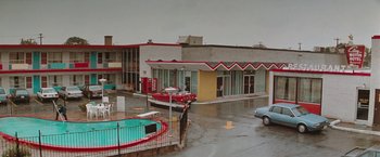 Movie still from “The Adjuster” (1991), directed by Atom Egoyan – A motel with a pool and a car parked in front of it; Extreme Wide shot, High angle