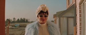 Movie still from “The Adjuster” (1991), directed by Atom Egoyan – A woman wearing a white hat and a blue coat; Close Up shot, Low angle