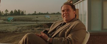 Movie still from “The Adjuster” (1991), directed by Atom Egoyan – A man sitting on a chair in a field; Close Up shot, Low angle