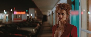 Movie still from “The Adjuster” (1991), directed by Atom Egoyan – A woman in a red dress standing in a hallway; Close Up shot, Over the shoulder angle