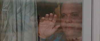 Movie still from “The Adjuster” (1991), directed by Atom Egoyan – A man is looking out a window at the camera; Close Up shot, Low angle