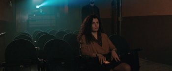 Movie still from “The Adjuster” (1991), directed by Atom Egoyan – A woman sitting in a movie theater holding a cell phone in her hand; Medium shot, Low angle