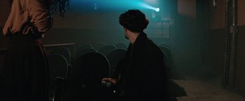 Movie still from “The Adjuster” (1991), directed by Atom Egoyan – A man standing in front of a row of chairs; Wide shot, Over the shoulder angle