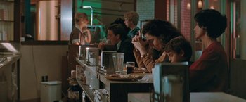 Movie still from “The Adjuster” (1991), directed by Atom Egoyan – A group of people sitting at a table in a restaurant; Medium shot, Over the shoulder angle