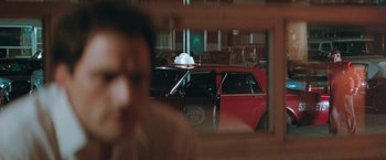 Movie still from “The Adjuster” (1991), directed by Atom Egoyan – A red car with a white hat sitting in front of a window; Close Up shot, Over the shoulder angle