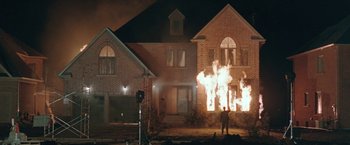Movie still from “The Adjuster” (1991), directed by Atom Egoyan – A man standing in front of a house on fire at night; Extreme Wide shot, Low angle