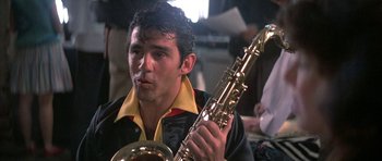 Movie still from “The Adventures of Buckaroo Banzai Across the 8th Dimension” (1984), directed by W.D. Richter – A man holding a saxophone while sitting in a room; Close Up shot, Over the shoulder angle