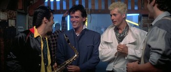 Movie still from “The Adventures of Buckaroo Banzai Across the 8th Dimension” (1984), directed by W.D. Richter – A group of men standing next to each other holding instruments; Medium shot, Over the shoulder angle