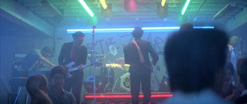 Movie still from “The Adventures of Buckaroo Banzai Across the 8th Dimension” (1984), directed by W.D. Richter – Two men are performing in front of a neon sign; Wide shot, Over the shoulder angle