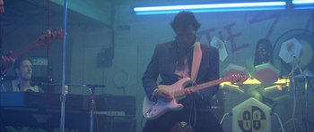 Movie still from “The Adventures of Buckaroo Banzai Across the 8th Dimension” (1984), directed by W.D. Richter – A man in a suit playing an electric guitar; Medium shot, Low angle