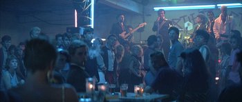 Movie still from “The Adventures of Buckaroo Banzai Across the 8th Dimension” (1984), directed by W.D. Richter – A group of people are gathered around a bar; Wide shot, Over the shoulder angle