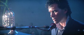 Movie still from “The Adventures of Buckaroo Banzai Across the 8th Dimension” (1984), directed by W.D. Richter – A man is speaking into a microphone at a podium; Close Up shot, Low angle