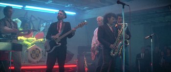 Movie still from “The Adventures of Buckaroo Banzai Across the 8th Dimension” (1984), directed by W.D. Richter – A group of men in suits and ties playing musical instruments; Wide shot, Low angle