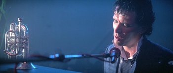 Movie still from “The Adventures of Buckaroo Banzai Across the 8th Dimension” (1984), directed by W.D. Richter – A man is sitting at a microphone in front of a microphone; Close Up shot, Low angle