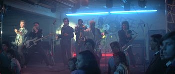 Movie still from “The Adventures of Buckaroo Banzai Across the 8th Dimension” (1984), directed by W.D. Richter – A group of people in a room with musical instruments; Wide shot, Low angle