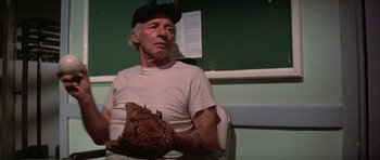 Movie still from “The Adventures of Buckaroo Banzai Across the 8th Dimension” (1984), directed by W.D. Richter – An older man holding a baseball glove in a room; Close Up shot, Low angle