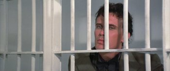 Movie still from “The Adventures of Buckaroo Banzai Across the 8th Dimension” (1984), directed by W.D. Richter – A man in a jail cell behind bars looking out; Close Up shot, Low angle