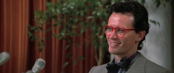 Movie still from “The Adventures of Buckaroo Banzai Across the 8th Dimension” (1984), directed by W.D. Richter – A man wearing red glasses and a bow tie; Close Up shot, Over the shoulder angle