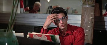 Movie still from “The Adventures of Buckaroo Banzai Across the 8th Dimension” (1984), directed by W.D. Richter – A man in a red shirt is looking at a book; Close Up shot, Low angle