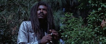 Movie still from “The Adventures of Buckaroo Banzai Across the 8th Dimension” (1984), directed by W.D. Richter – A man with dreadlocks holding a knife in his hand; Medium shot, Low angle