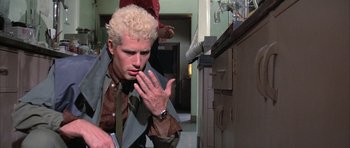 Movie still from “The Adventures of Buckaroo Banzai Across the 8th Dimension” (1984), directed by W.D. Richter – A man with blonde hair is looking down at his hand; Close Up shot, Low angle