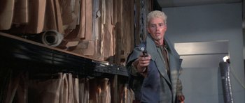 Movie still from “The Adventures of Buckaroo Banzai Across the 8th Dimension” (1984), directed by W.D. Richter – A man holding a cell phone while standing in front of a wall; Medium shot, Low angle