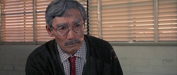 Movie still from “The Adventures of Buckaroo Banzai Across the 8th Dimension” (1984), directed by W.D. Richter – An old man with a beard and mustache wearing glasses and wearing a tie; Close Up shot, Over the shoulder angle