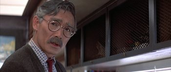 Movie still from “The Adventures of Buckaroo Banzai Across the 8th Dimension” (1984), directed by W.D. Richter – An older man wearing glasses and a tie; Close Up shot, Over the shoulder angle