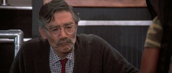 Movie still from “The Adventures of Buckaroo Banzai Across the 8th Dimension” (1984), directed by W.D. Richter – An older man wearing glasses and wearing a tie; Close Up shot, Over the shoulder angle