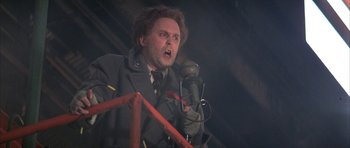 Movie still from “The Adventures of Buckaroo Banzai Across the 8th Dimension” (1984), directed by W.D. Richter – A man in a military jacket is holding a microphone; Close Up shot, Low angle
