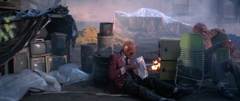 Movie still from “The Adventures of Buckaroo Banzai Across the 8th Dimension” (1984), directed by W.D. Richter – A man sitting on the ground next to a pile of trash; Wide shot, High angle