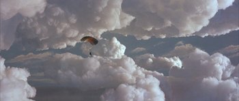 Movie still from “The Adventures of Buckaroo Banzai Across the 8th Dimension” (1984), directed by W.D. Richter – A parachutist is in the sky above the clouds; Extreme Wide shot, Overhead angle