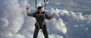 Movie still from “The Adventures of Buckaroo Banzai Across the 8th Dimension” (1984), directed by W.D. Richter – A man in a parachute is flying through the sky; Medium shot, Low angle