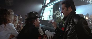 Movie still from “The Adventures of Ford Fairlane” (1990), directed by Renny Harlin – Two men are sitting in a car and one of them is holding flowers; Medium shot, Over the shoulder angle