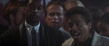 Movie still from “The Adventures of Ford Fairlane” (1990), directed by Renny Harlin – A group of men standing next to each other in a room; Close Up shot, Low angle