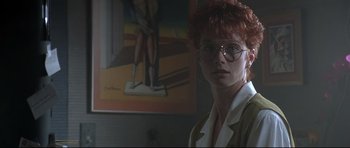 Movie still from “The Adventures of Ford Fairlane” (1990), directed by Renny Harlin – A woman with red hair wearing glasses in front of a painting; Close Up shot, Low angle