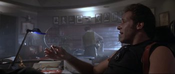 Movie still from “The Adventures of Ford Fairlane” (1990), directed by Renny Harlin – A man sitting at a table in front of a window; Medium shot, Low angle