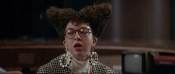 Movie still from “The Adventures of Ford Fairlane” (1990), directed by Renny Harlin – A woman with a large hair wig on top of her head; Close Up shot, Over the shoulder angle