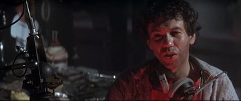 Movie still from “The Adventures of Ford Fairlane” (1990), directed by Renny Harlin – A man in a red shirt is standing in a dark room; Close Up shot, Low angle