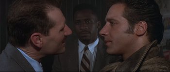 Movie still from “The Adventures of Ford Fairlane” (1990), directed by Renny Harlin – Two men in suits and a man in a suit looking at each other in front of another man in a suit and tie; Close Up shot, Over the shoulder angle