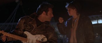 Movie still from “The Adventures of Ford Fairlane” (1990), directed by Renny Harlin – A man and a woman are holding a guitar; Medium shot, Low angle