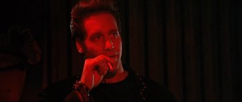 Movie still from “The Adventures of Ford Fairlane” (1990), directed by Renny Harlin – A man in a black shirt is looking at the camera; Close Up shot, Over the shoulder angle