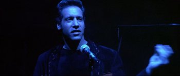 Movie still from “The Adventures of Ford Fairlane” (1990), directed by Renny Harlin – A man standing in front of a microphone on a stage; Close Up shot, Low angle