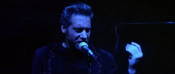 Movie still from “The Adventures of Ford Fairlane” (1990), directed by Renny Harlin – A man with a beard is singing into a microphone; Close Up shot, Low angle