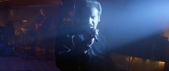 Movie still from “The Adventures of Ford Fairlane” (1990), directed by Renny Harlin – A man is singing into a microphone in a dark room; Close Up shot, Low angle
