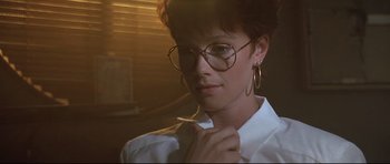 Movie still from “The Adventures of Ford Fairlane” (1990), directed by Renny Harlin – A woman in glasses and a white shirt is smoking a cigarette; Close Up shot, Low angle