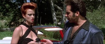 Movie still from “The Adventures of Ford Fairlane” (1990), directed by Renny Harlin – A man and a woman standing next to each other in front of trees; Medium shot, Over the shoulder angle