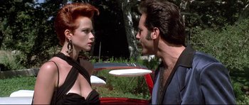 Movie still from “The Adventures of Ford Fairlane” (1990), directed by Renny Harlin – A man and a woman standing next to each other in front of a red car; Medium shot, Low angle